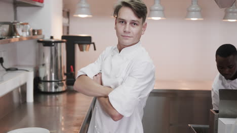 portrait of happy caucasian male chef crossing arms and smiling in kitchen, copy space, slow motion