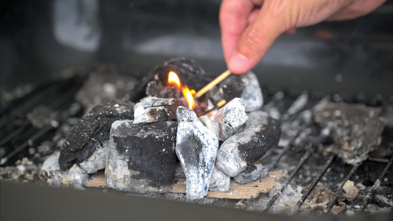 movimiento lento de una mano masculina quemando un fósforo mientras enciende un fuego usando carbón para una parrilla