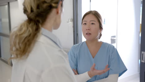 serious diverse female doctors discussing in hospital corridor, slow motion