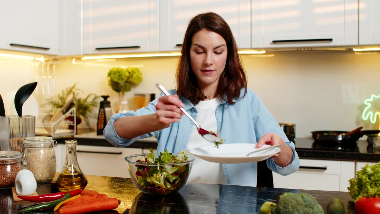 Young woman adds olive oil dressing to fresh salad in home kitchen for healthy diet weight loss meal
