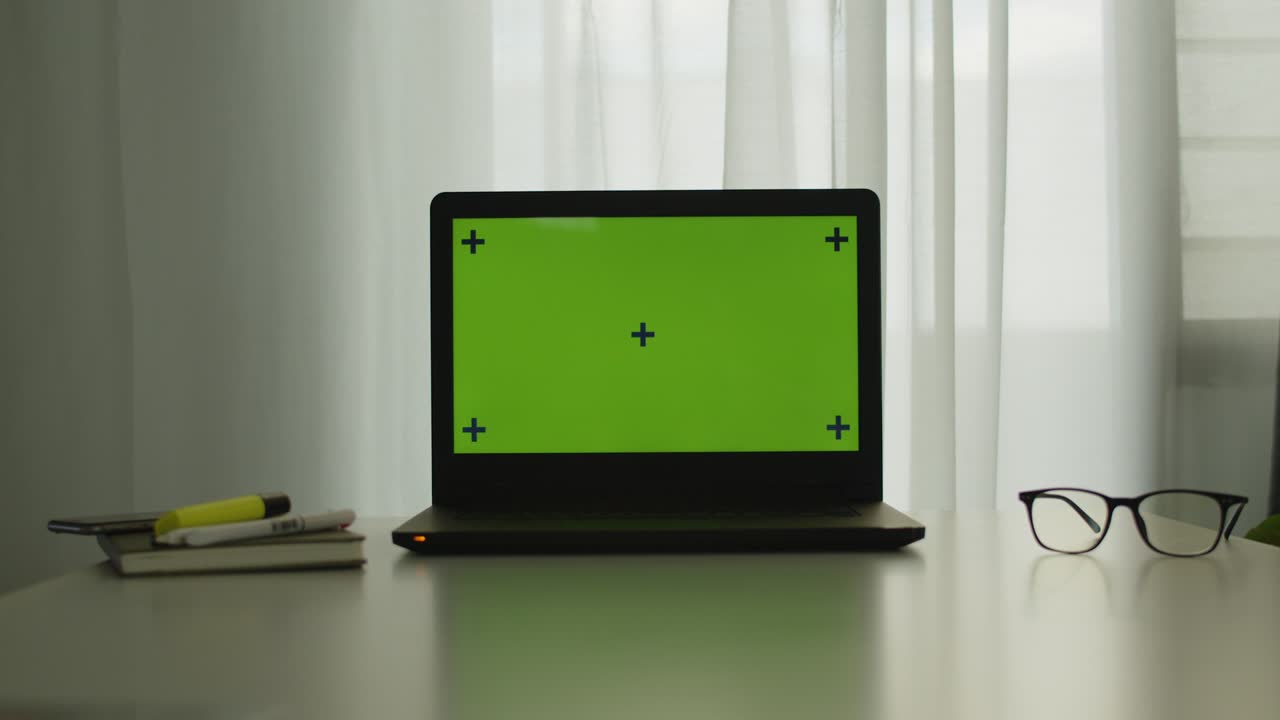 Shot of a laptop with chroma key green screen on a table in office room, watching online content, communications, video conference concept.