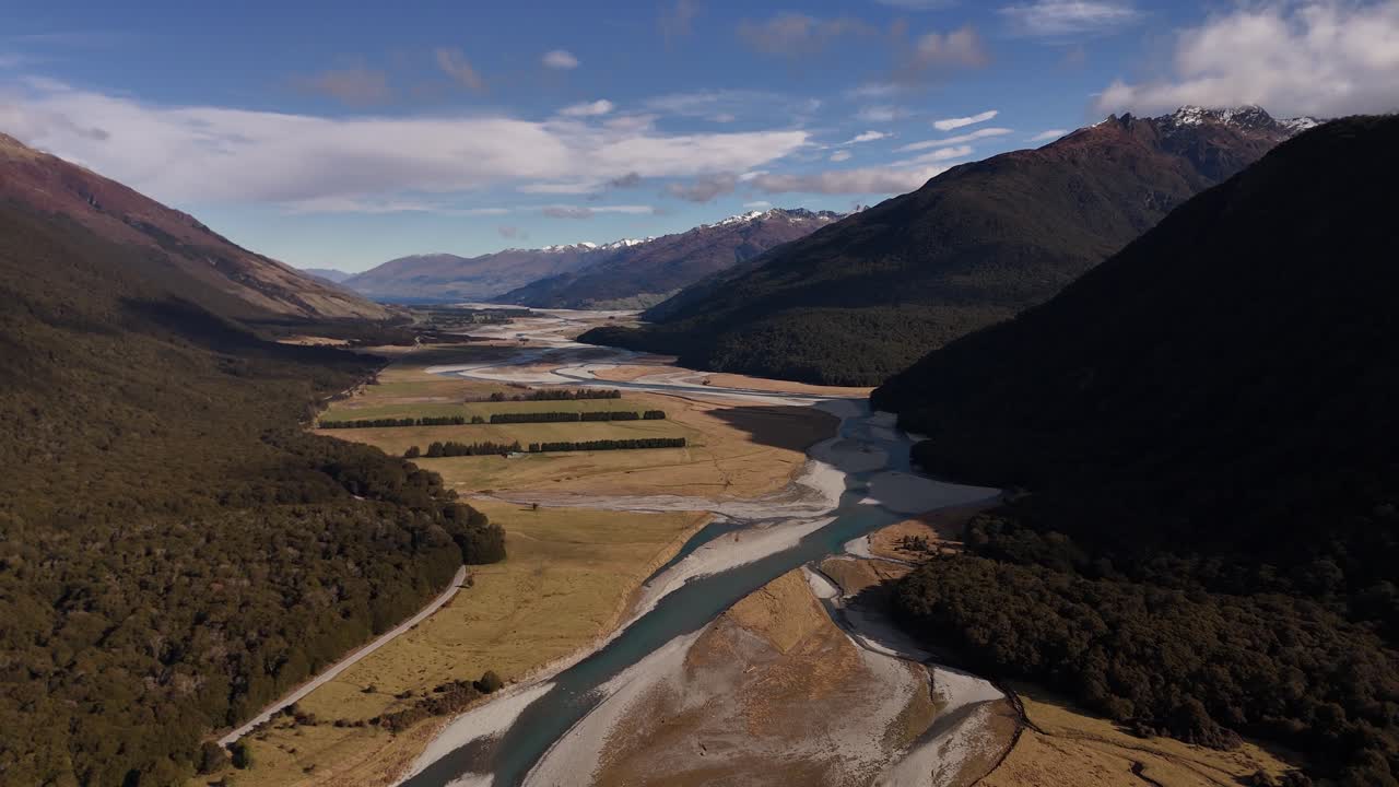 Ripresa aerea di un fiume tra le montagne in una giornata di sole in Nuova Zelanda. Cima innevata di una montagna in lontananza. Campo lungo. Natura pacifica della Nuova Zelanda.