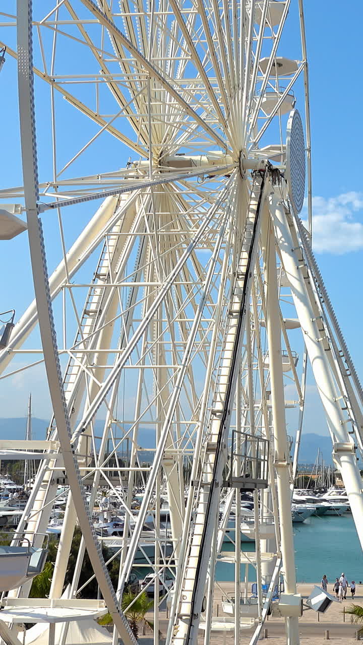 Side view of white ferris wheel rotating in Antibes, France. Vertical