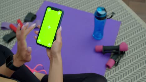 fitness woman use smartphone with green screen after training at home. healthy lifestyle. stretching, leaning forward. training on distance.