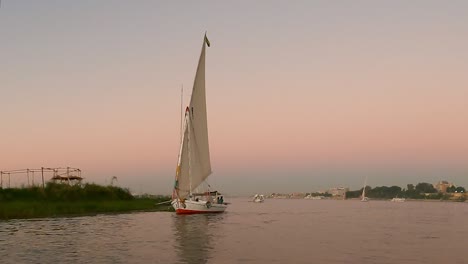 Beautiful-River-scape-with-felucca-boats-on-Nile-river-in-Luxor-with-sunset-colors-reflecting-on-water,-Egypt