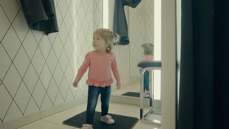 Kleines-Mädchen-Geht-In-Den-Raum,-Um-Kleidung-Im-Laden-Anzuprobieren-Und-Schaut-In-Den-Spiegel