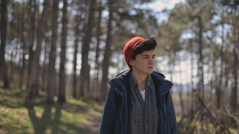 a young woman with short hair in a red woolen hat walks through the forest looking from side to side