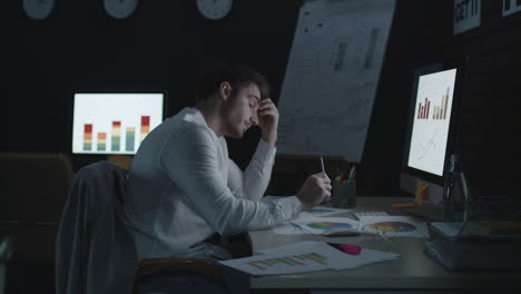 upset business man looking financial reports in night office.