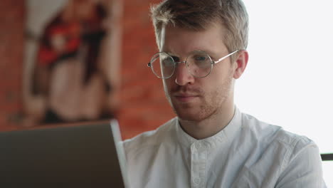 handsome european man with glasses is working with laptop in cafe freelancer is surfing internet for looking information