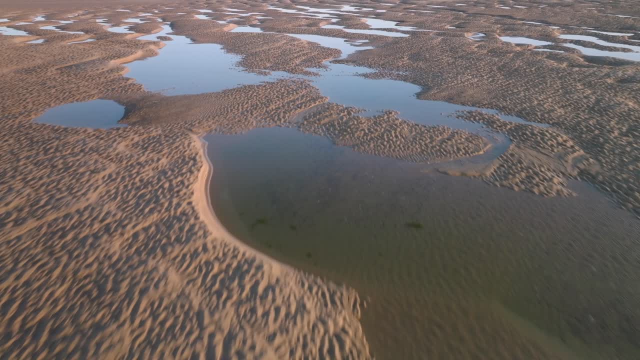 Seawater pools and tidal sand patterns at golden hour. Low fast flight over.
