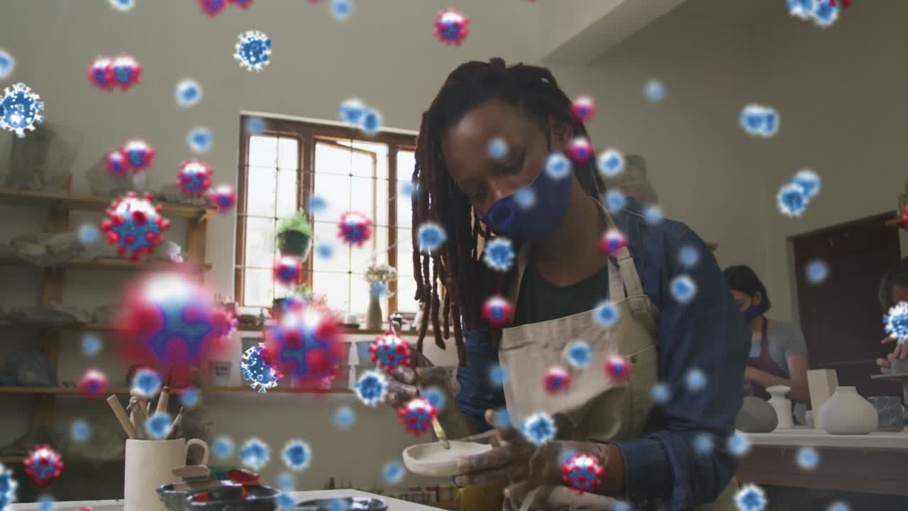 animazione di cellule di covid-19 su donne e uomini che lavorano in uno studio di ceramica indossando maschere facciali