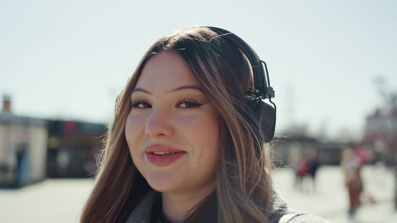 Donna gioiosa all'aperto. Donna sorridente in ambiente urbano. Giovane donna allegra con le cuffie all'aperto. Donna soddisfatta con le cuffie che vive una giornata di sole tra le vivaci strade della città.