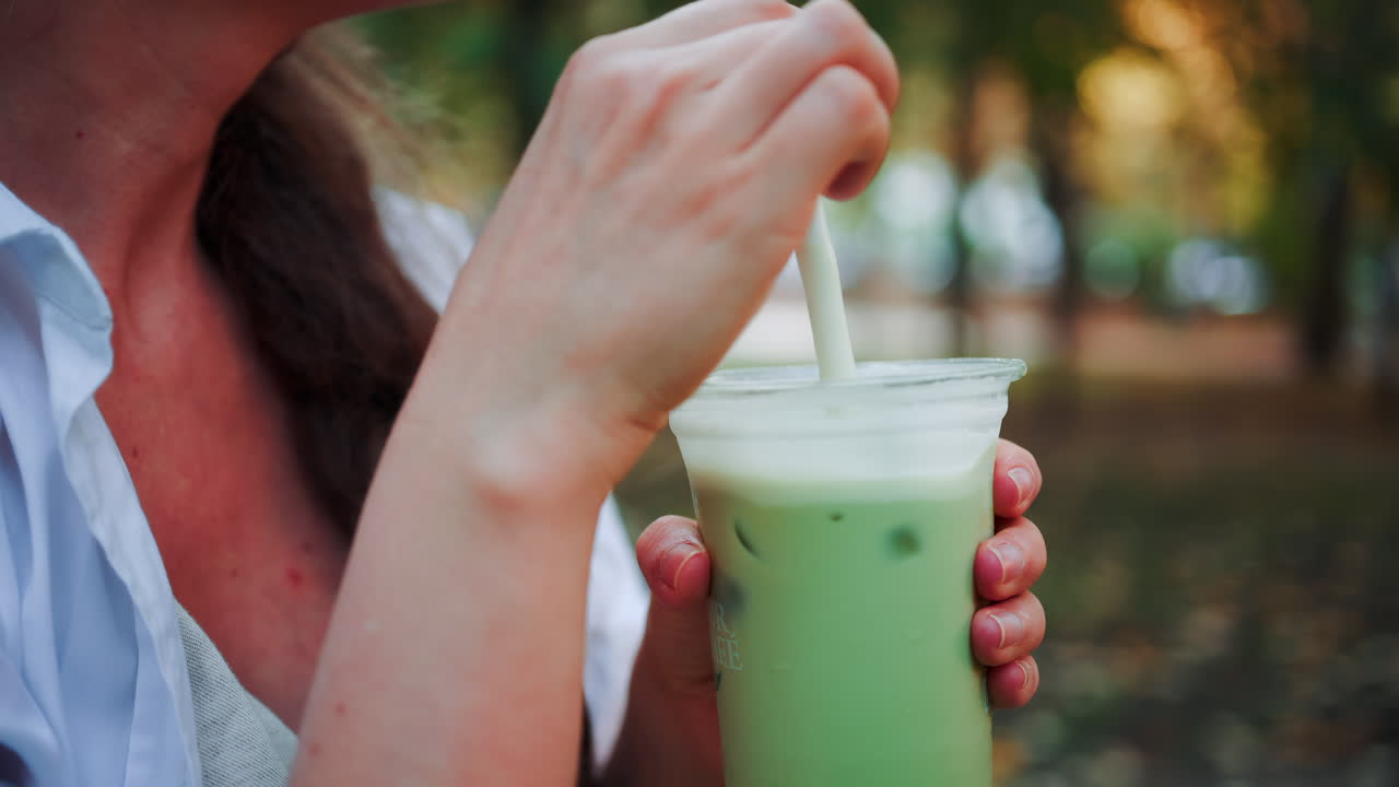 Close up of woman's hand holding an iced matcha latte outdoors