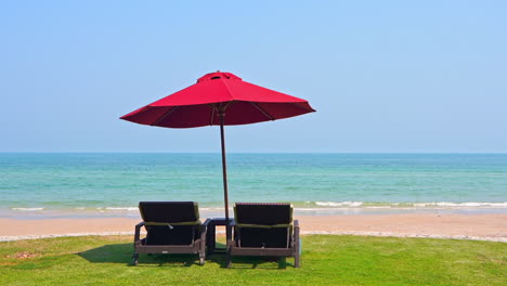 Two-Deck-chairs-Under-Parasol-on-green-grass-part-of-the-beach-lounge-seafront-daytime