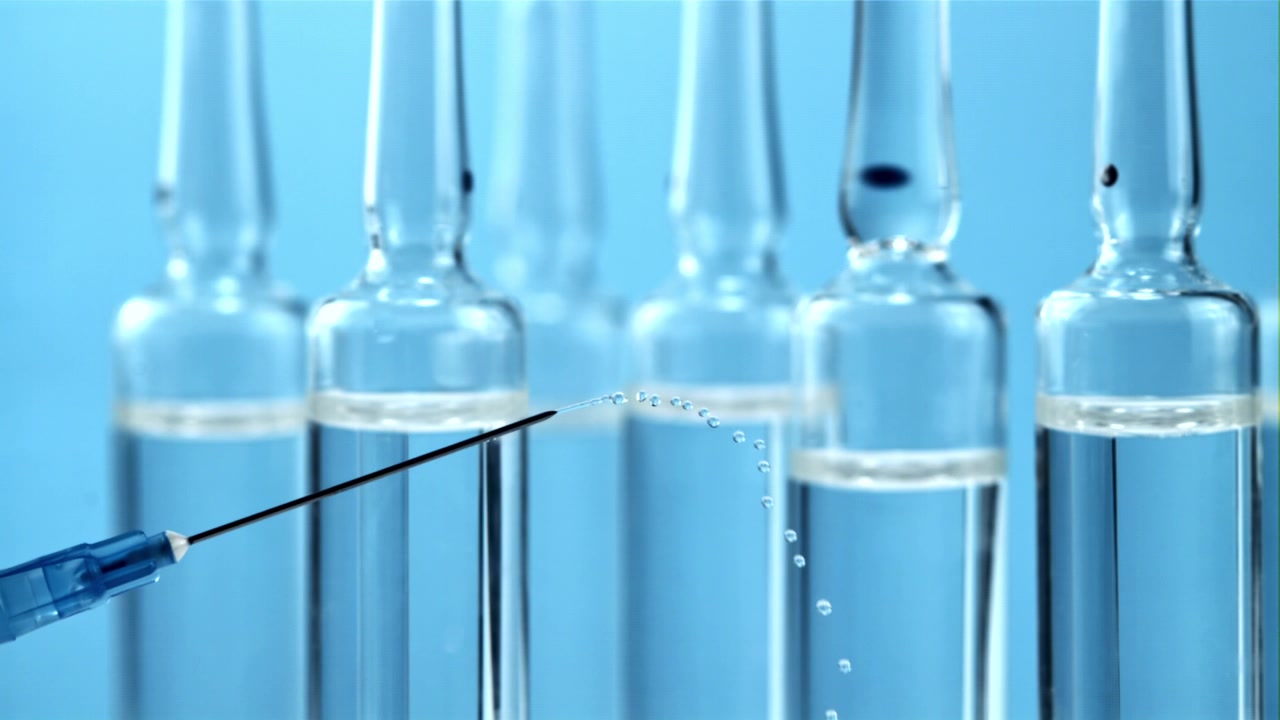 Primo piano di un ago di siringa che espelle gocce di liquido trasparente.
