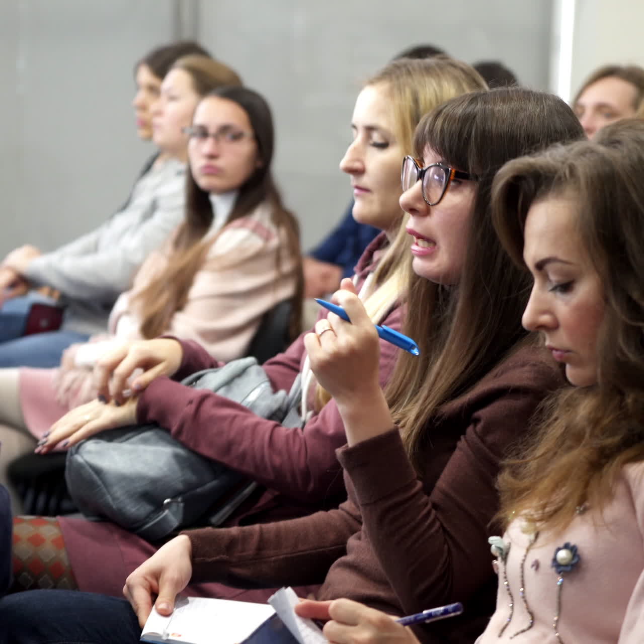 Listeners at modern forum. Young women are sitting in the audience and listening to the speech at the conference meeting.