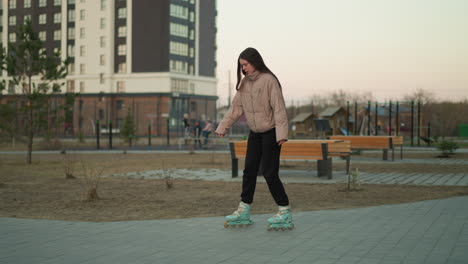 a young girl, dressed in a peach jacket and black trousers, rollerblades along a paved path in a serene park setting. the background features benches and a calm, outdoor environment