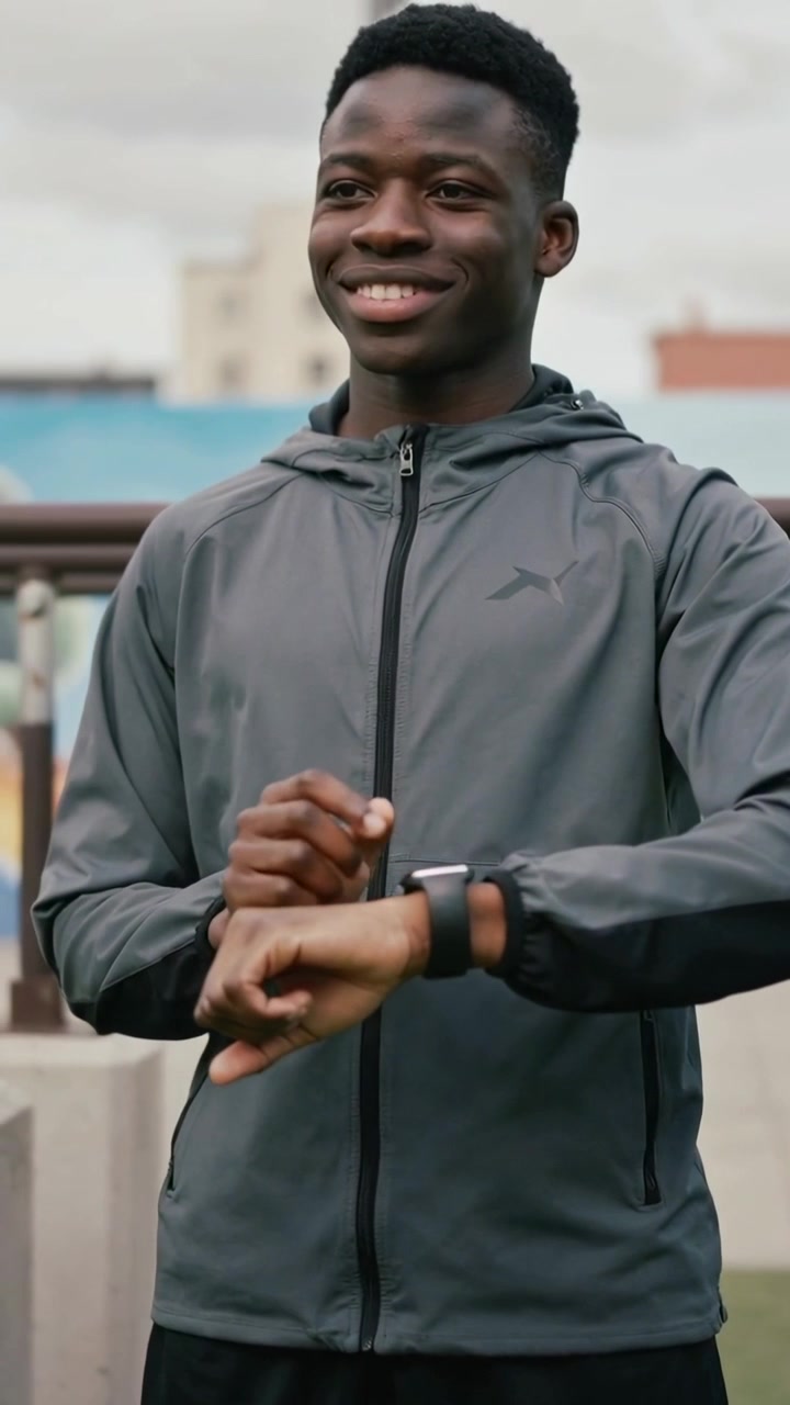 Vertical video: Glancing at left wrist, man in gray jacket tapping watch at park, checking run time