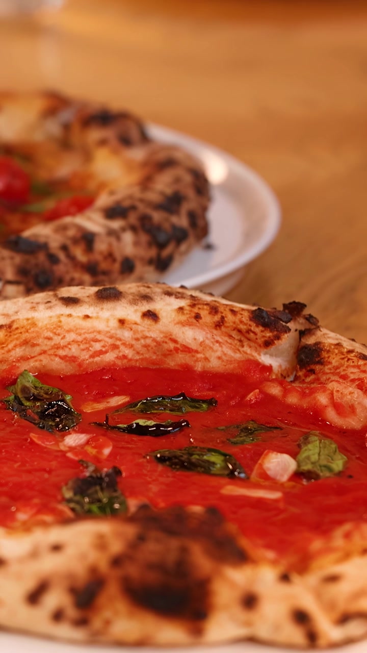 Panoramica ravvicinata di pizze gourmet con croste carbonizzate e basilico fresco su un tavolo di legno.