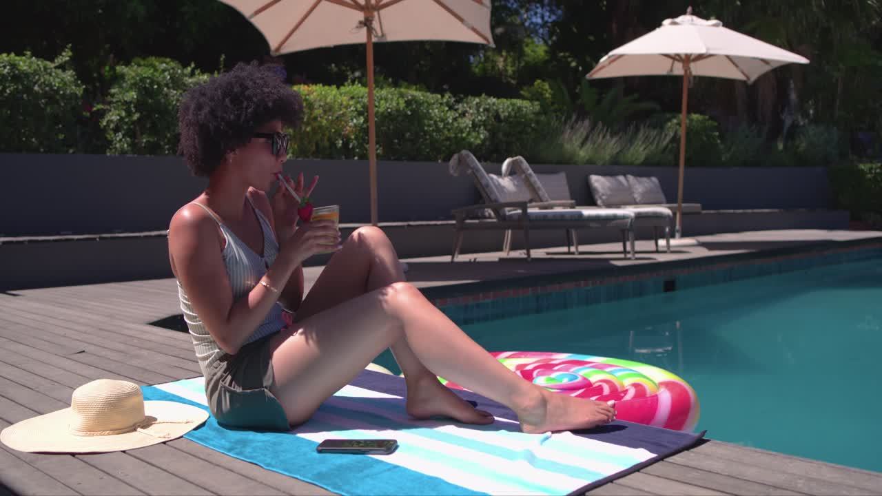 Sun is causing woman to tilt face up while sipping cold drink for sunbathing by pool