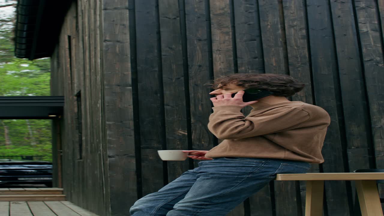 hombre hablando por teléfono mientras disfruta de café fuera de una cabaña