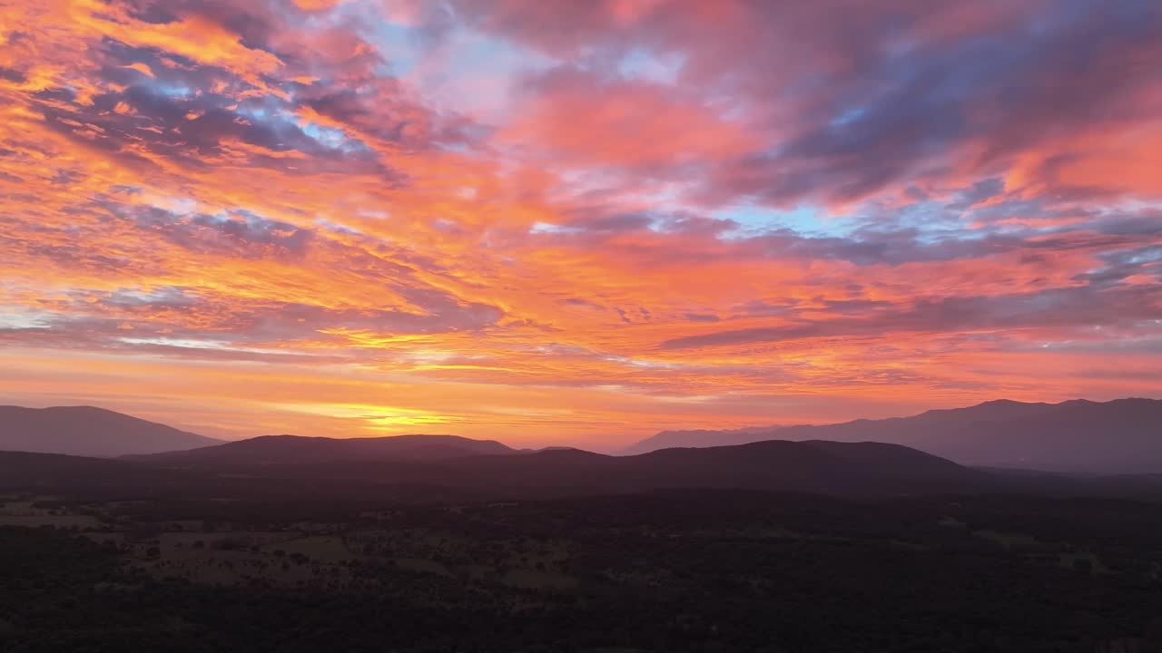 vuelo al atardecer en un valle visualizando en un ligero giro a la derecha las montañas y bosques y un cielo espectacular con una increíble gama de colores azul, rojo amarillo naranja en ávila-españa