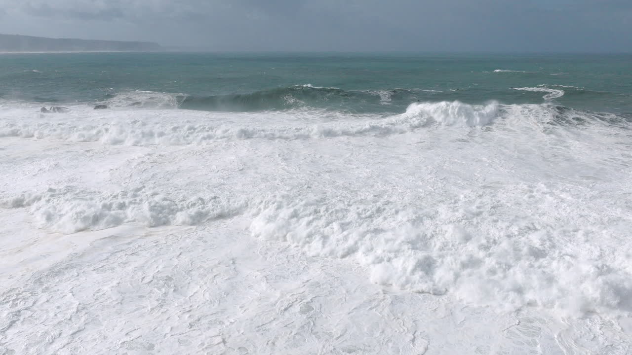Aerial drone shot of huge storm waves coming into shore on a day with giant waves in Nazaré, Portugal, Europe. Jet ski riders and surfers in Atlantic Ocean