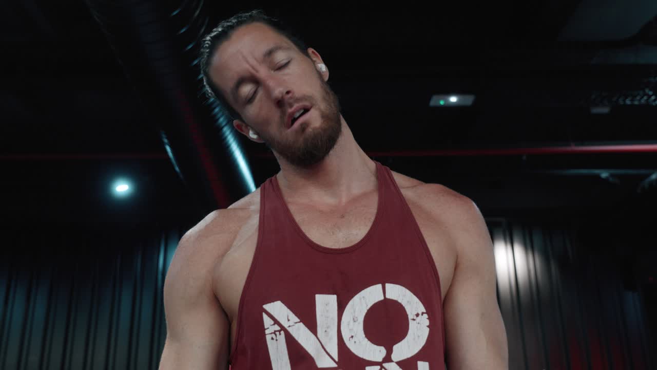 Fixed shot from the front of a handsome, muscular young Caucasian man doing weight training, lifting weights with his arms to build his shoulders