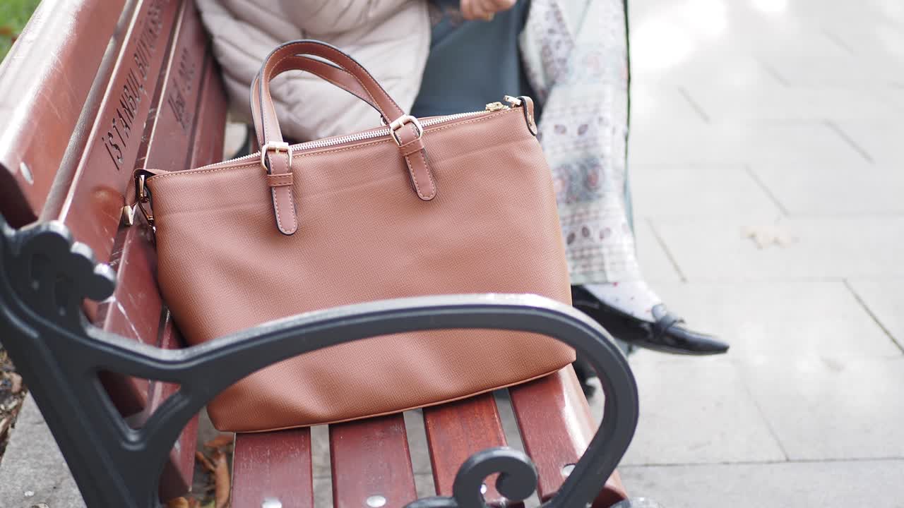 갈색 드백 을 들고 공원 벤치 에 앉아 있는 여자