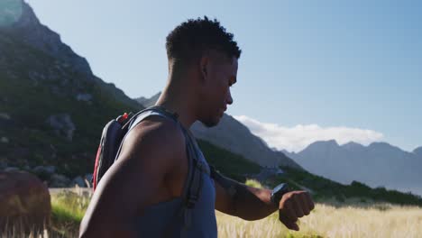 african american man cross country running in mountain countryside using smartwatch