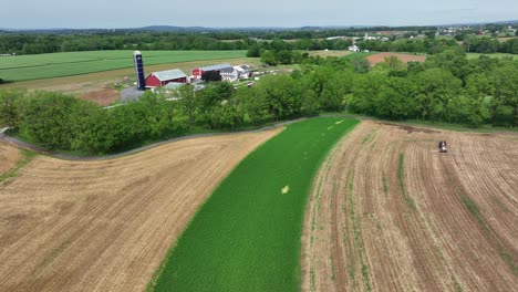 drone shot of american countryside with farm fields and silo storage. wild bees flying into camera lens. sunny day in summer. working tractor harvester on cropland.