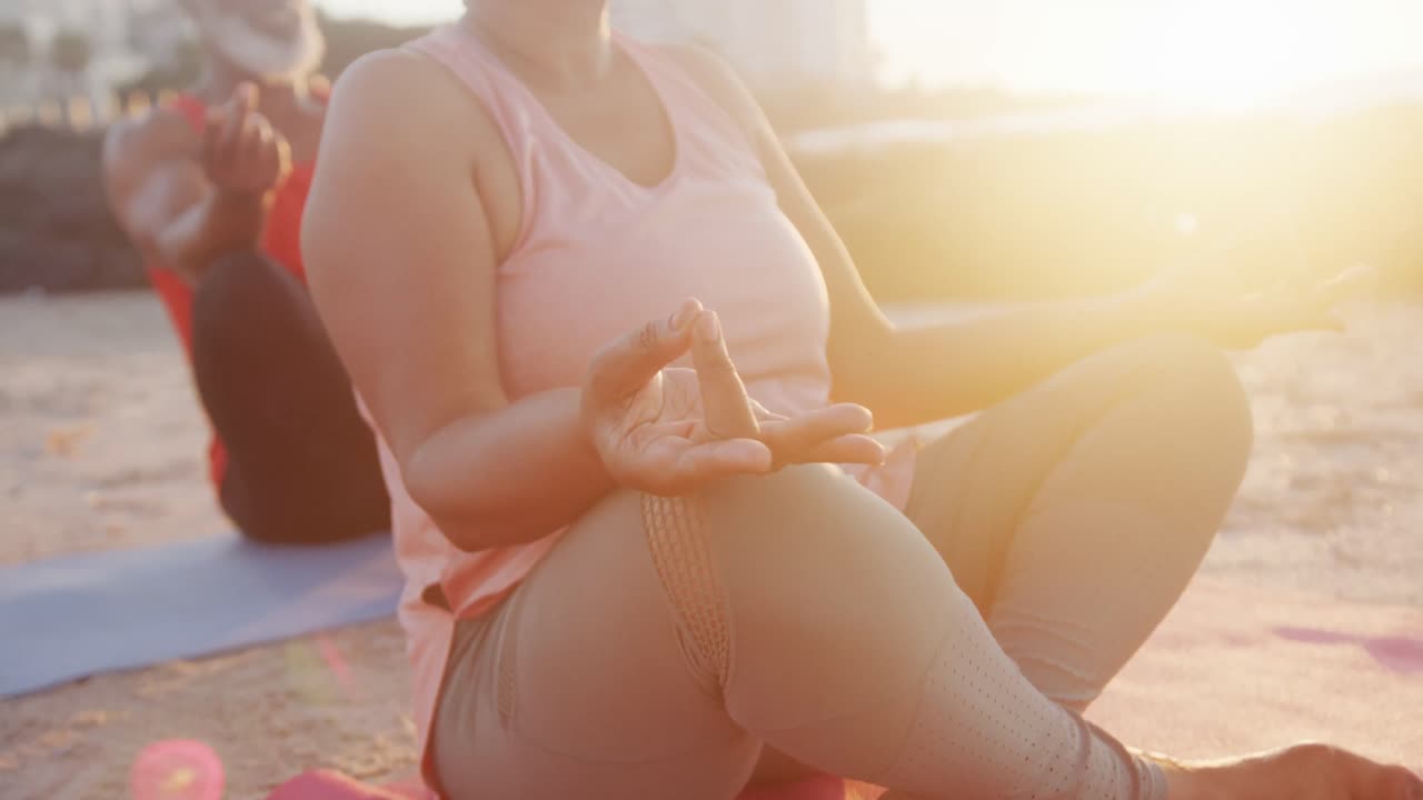 Coppia anziana afroamericana felice che fa yoga, meditando in spiaggia, al rallentatore