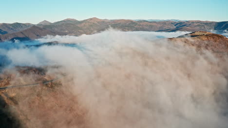 Wolken,-Die-über-Berggipfel-Rollen-Und-Ein-Heiteres,-Majestätisches-Gefühl-Vermitteln,-Aufgenommen-In-Einer-Luftaufnahme-Bei-Tag