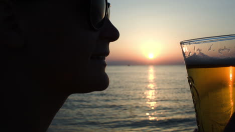 mujer bebiendo cerveza en la playa al atardecer
