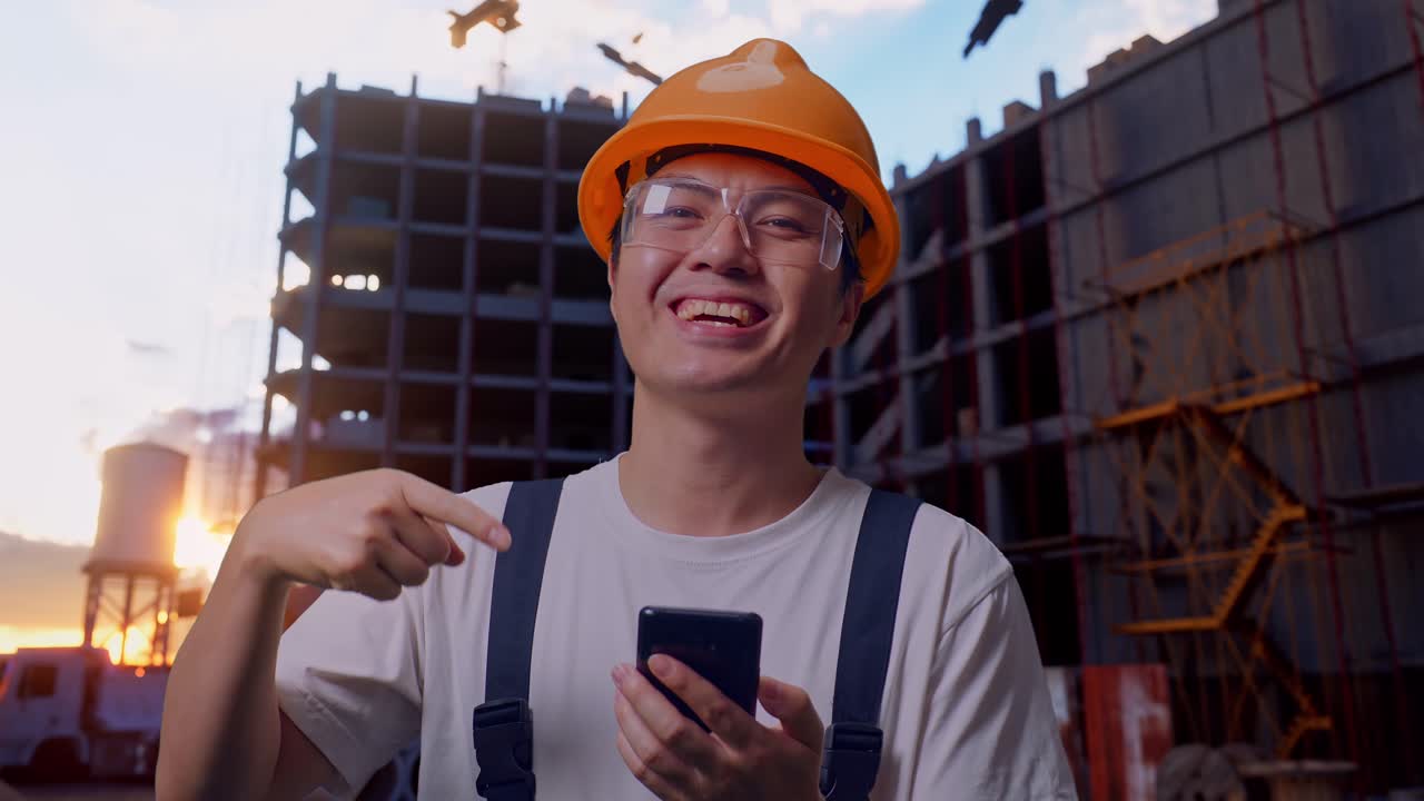 Asian Man Worker Pointing To Smartphone In His Hand At Construction Site