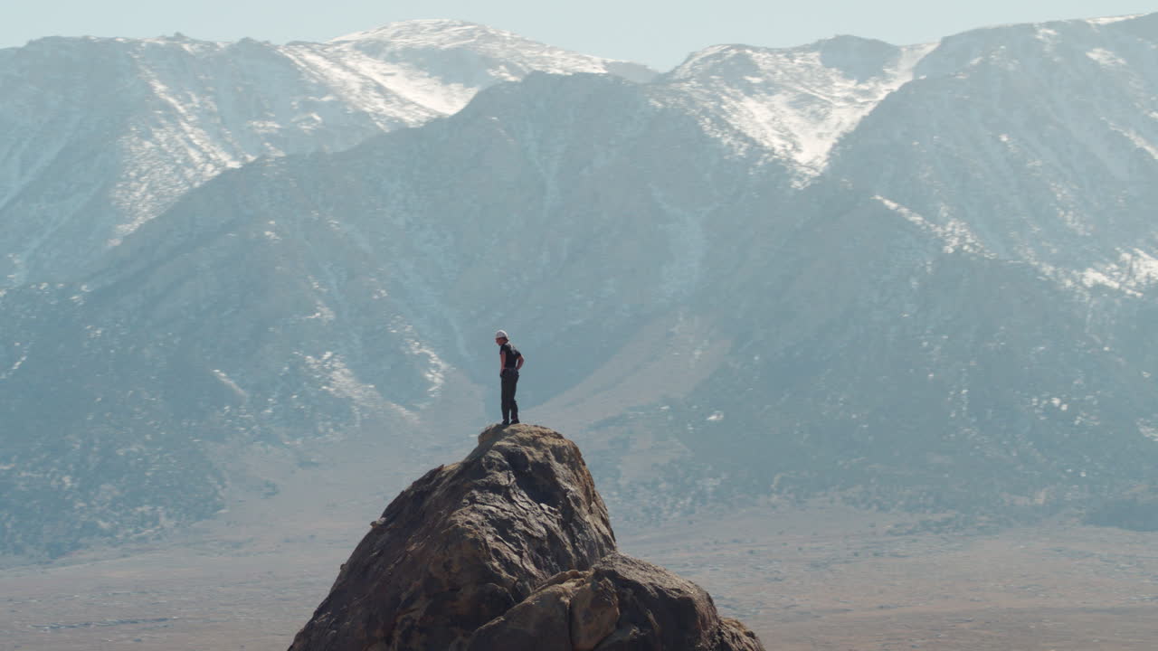 거대한 산을 바라보며 바위 정상에 서 있는 모험을 좋아하는 젊은 등산객