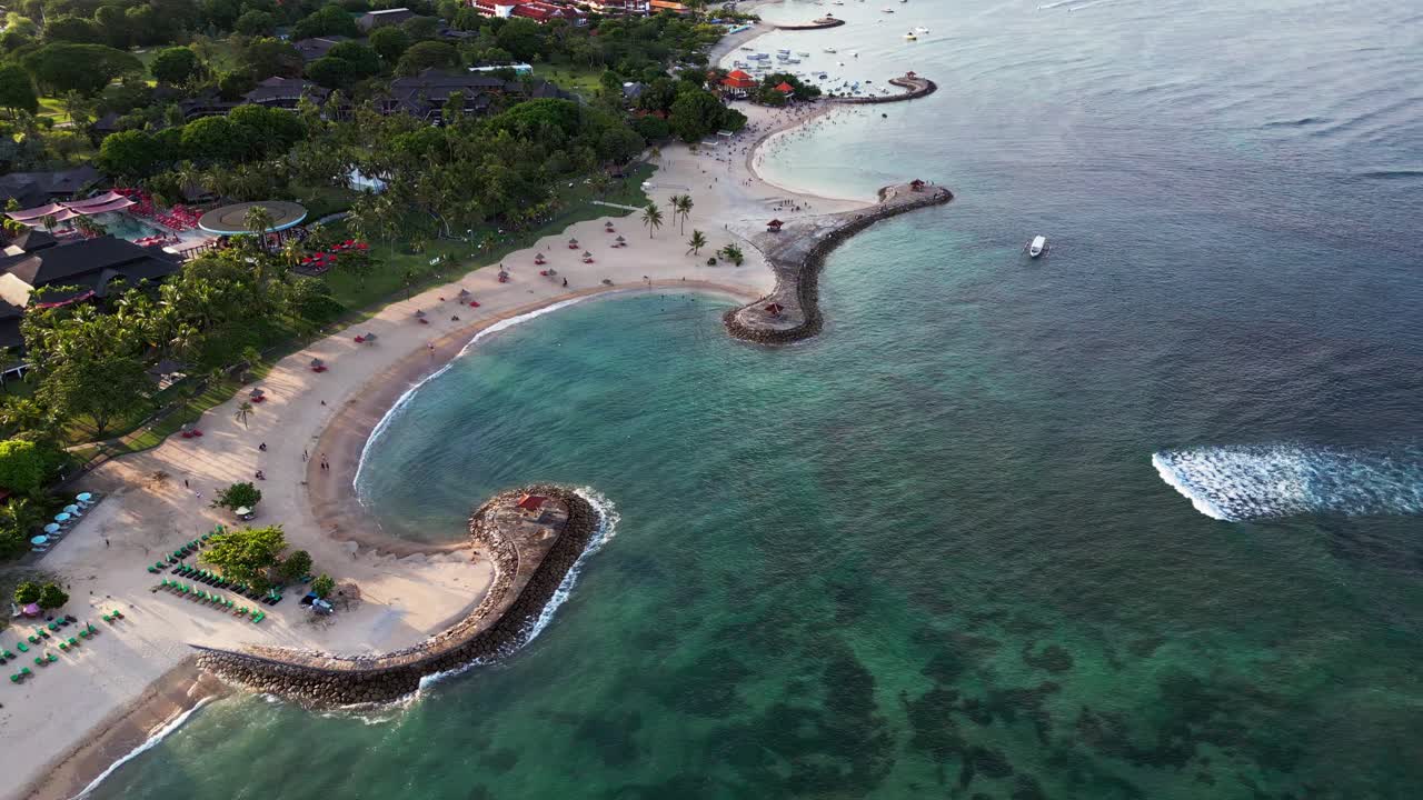 Aerial drone view shows Nusa Dua with curved white sand beaches clear reef water lined jetties and nearby resorts capturing the coastal layout and shoreline activity across this Bali tourism area