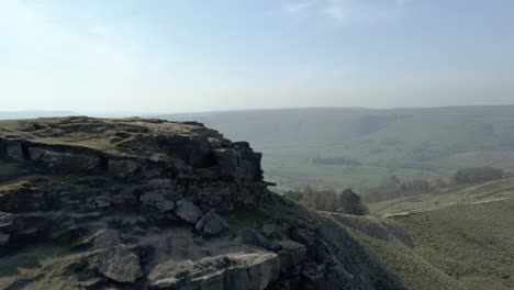 aerial shot showing the cliff face and rocks at the top of a hill walk in the hope valley area of the peak district, uk