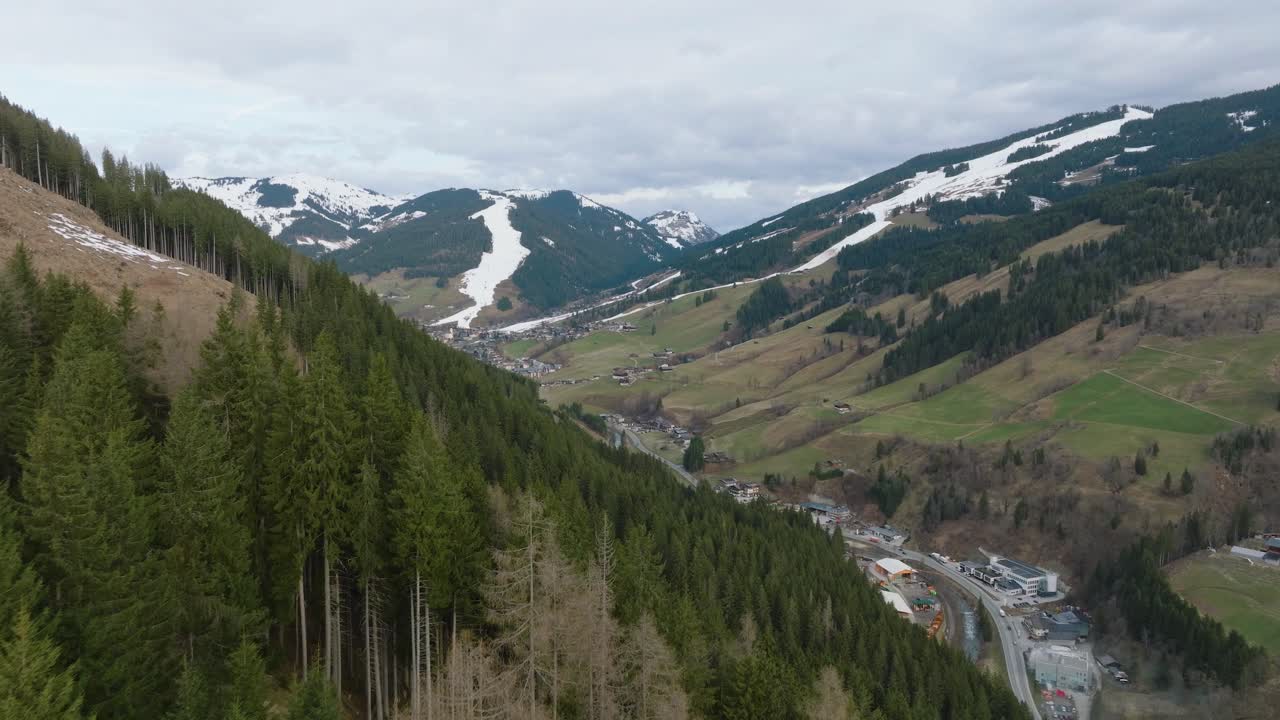 los pinos verdes y exuberantes que enmarcan una pintoresca estación de esquí austriaca en saalbach-hinterglemm, rastros de nieve en las laderas, vista aérea
