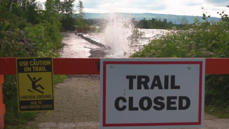 water crashing into a bulwark behind a sign that says "trail closed" in slow motion