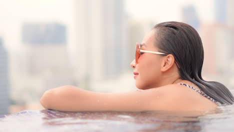 close up of young asian woman on rooftop infinity pool with amazing view of city in background, full frame