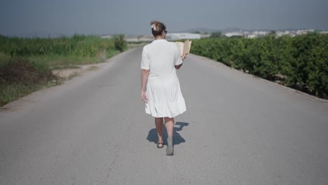 woman walking on a country road with a book