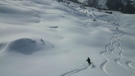 Aerial-following-young-sports-skier-down-snow-covered-glacier-mountain-range-slope-in-snowy-alpine-scenery