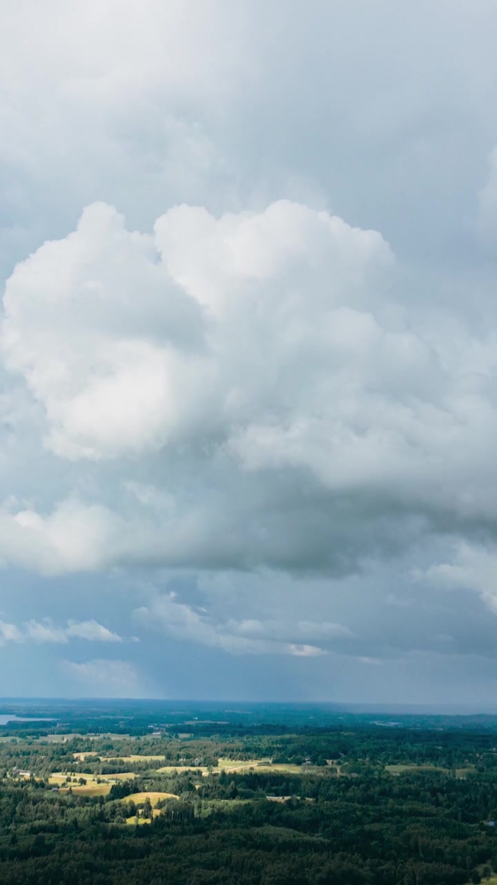 Vertical drone hyperlapse view of dramatic stormy rain clouds moving over a vast green countryside landscape and distant lake.