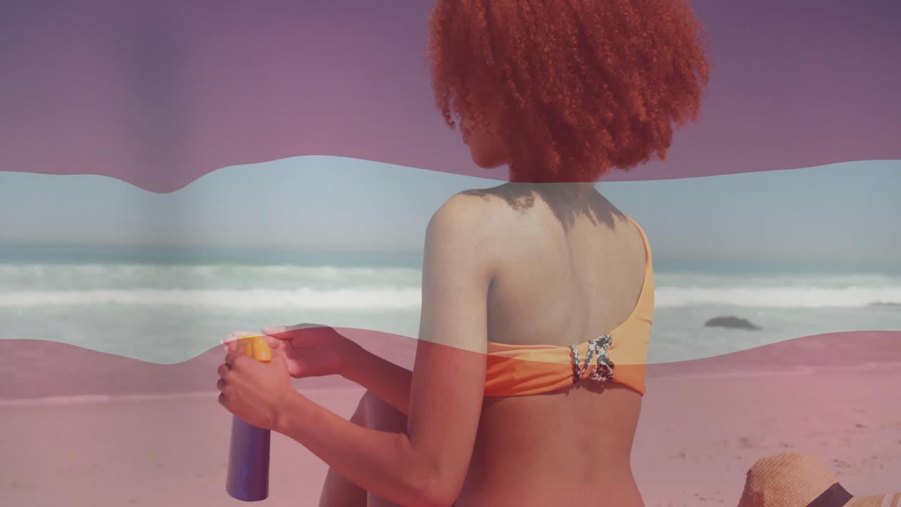 Holding sunscreen, woman in orange swimsuit at sunny beach with waves
