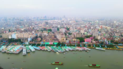 Aerial-view-across-Dhaka-cargo-ships-travelling-down-river-passing-colourful-Bangladesh-congested-mega-city