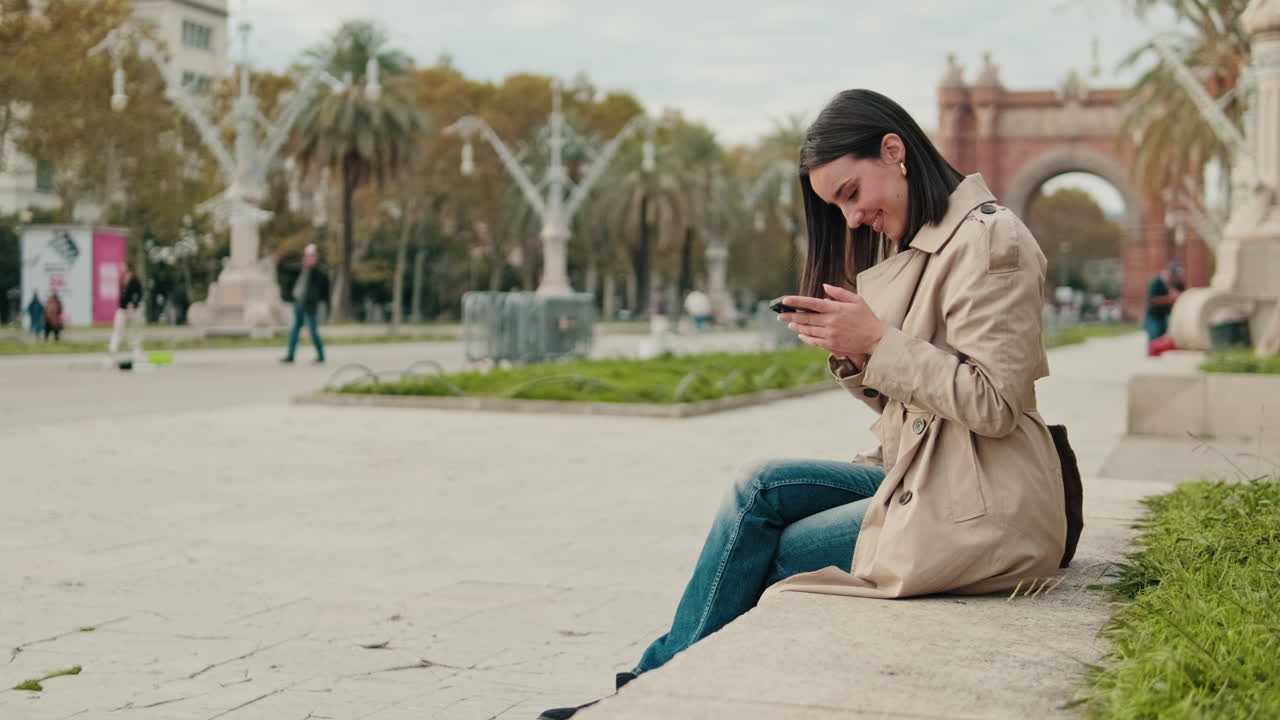 Young Woman Smiling and Texting on Smartphone in City Park