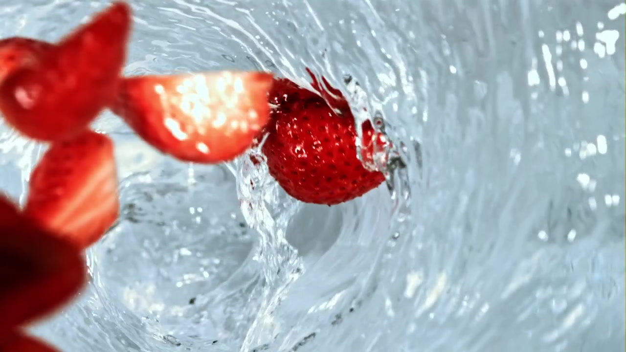 Fragole fresche e fette che schizzano in un vortice d'acqua limpida al rallentatore