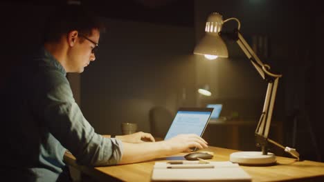 professional man sitting at his desk in office studio working on a laptop in the evening. man working with data, analyzing statistics, writing down information. 360 degree tracking arc shot movement