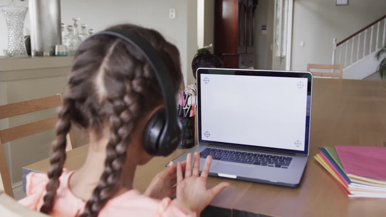 chica biracial aprendiendo en línea en la mesa usando portátil con espacio de copia en la pantalla, cámara lenta